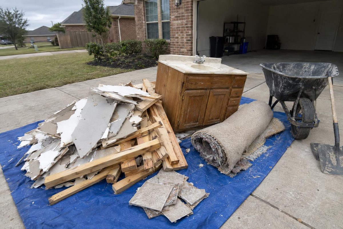 Broken drywall, cut lumber and an old vanity piled on a tarp in a driveway