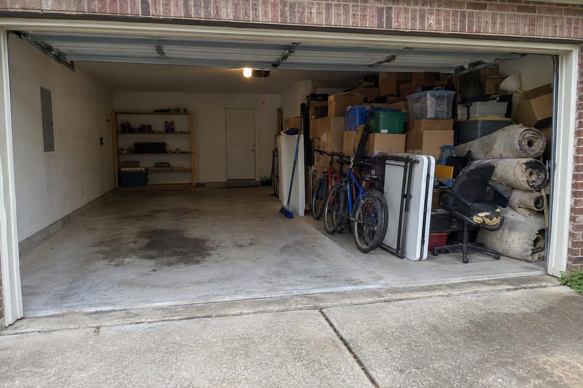 A two-car garage with one side cleared to the concrete and the other still stacked with boxes and bikes